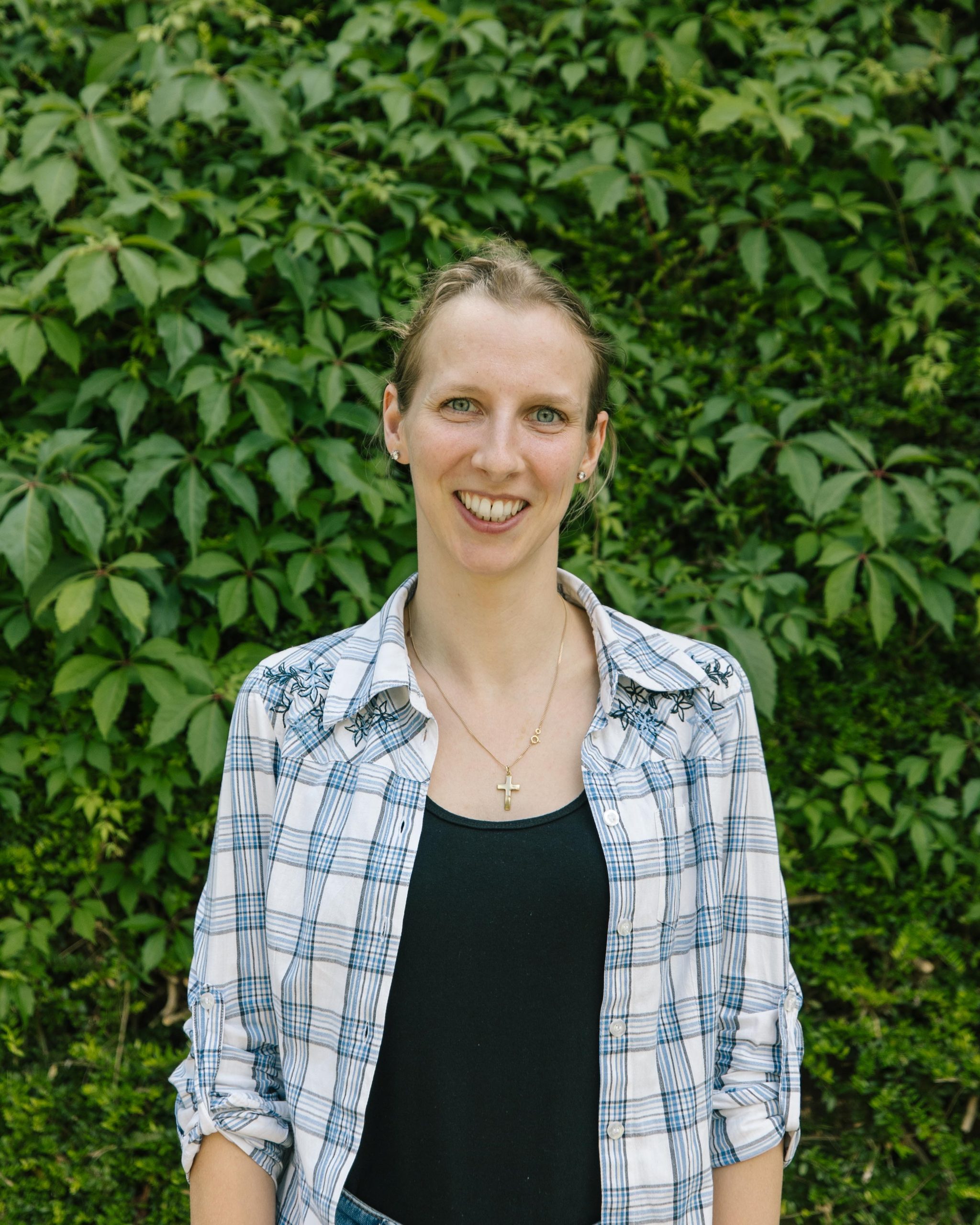 Eine junge Frau in der Mitte des Bildes. Hinter ihr sind grüne Blätter zu sehen